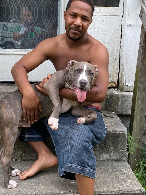 Man sitting on steps, hugging a grey pit bull with a tongue out