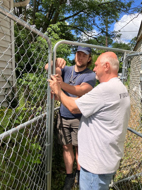 Two men installing a chain-link fence gate