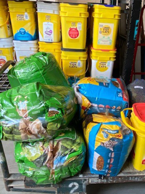 Large bags of dog food and multiple containers of sand litter stacked in a storage area