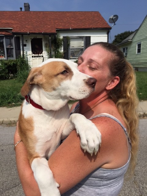 Woman holding a tan and white dog close to her face in front of a house