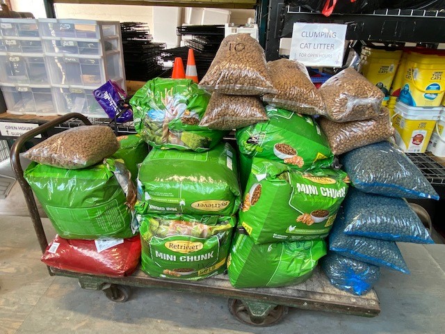 Large bags of Retriever Mini Chunk dog food and bags of kibble stacked on a cart in a storage area