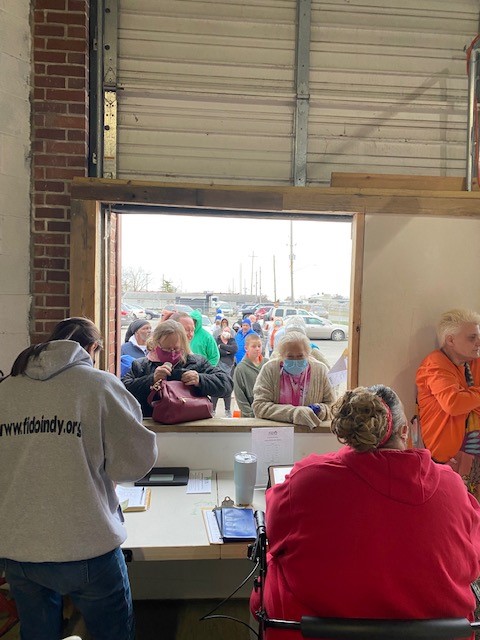 People waiting in line outside while volunteers inside assist them at the FIDO Indy facility